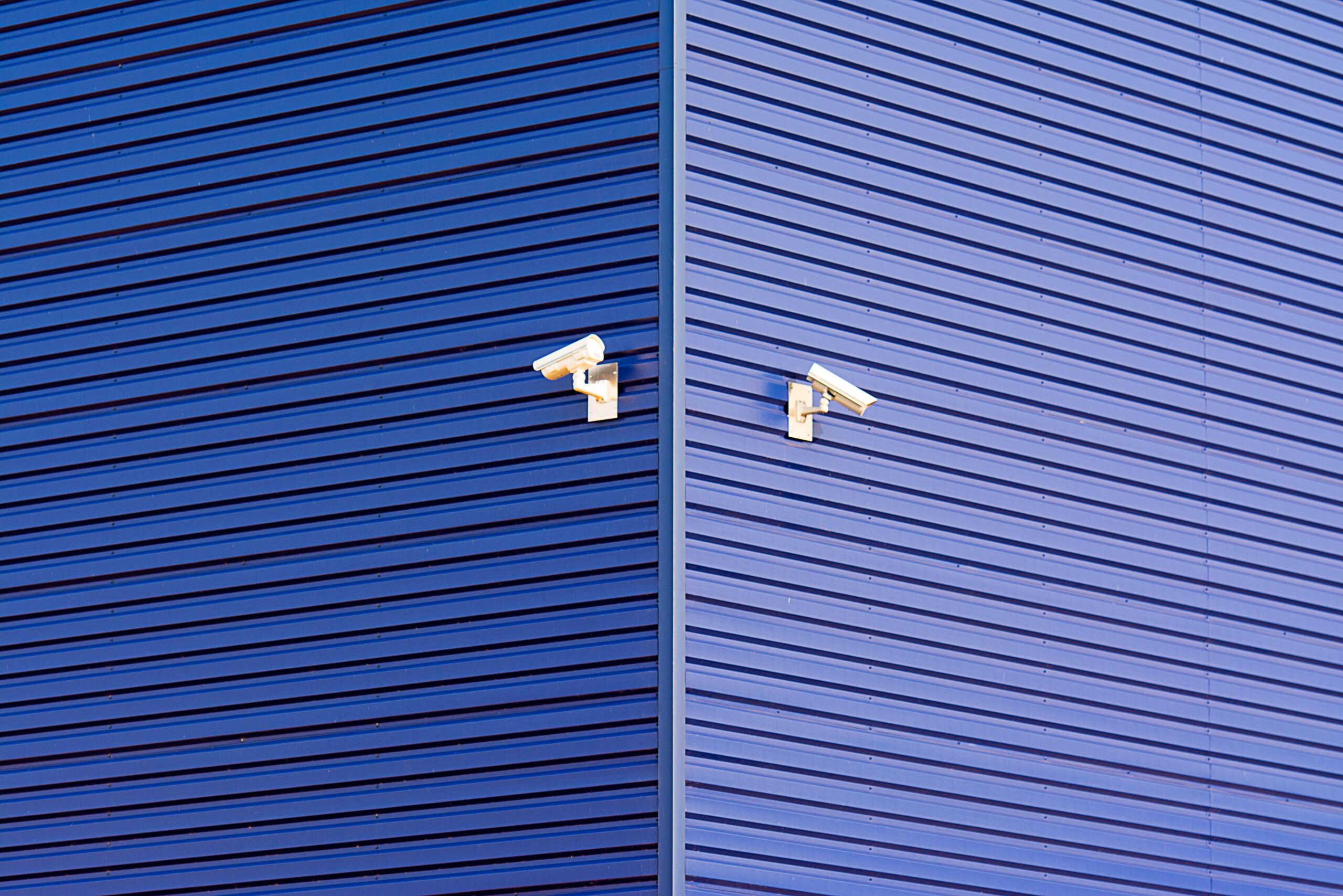 Minimalist image of a blue wall with two CCTV cameras emphasizing security and technology.
